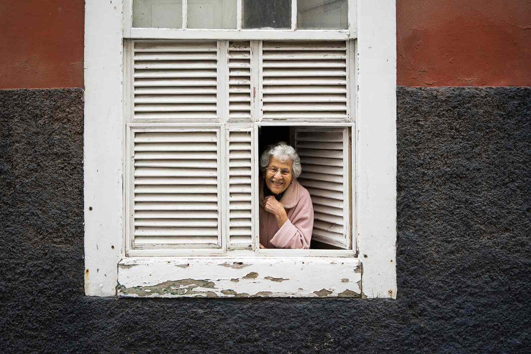 Femme agée qui sourit en ayant ouvert ses vollets le matin au réveil.